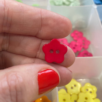 Red button held between fingers with a container of colorful buttons in the background