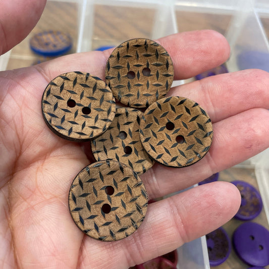 Hand holding four wooden buttons with a woven pattern, blurred container of buttons in the background.