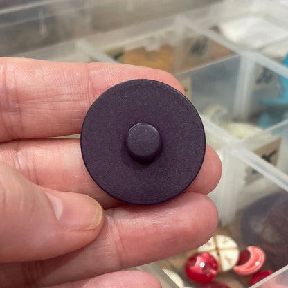 Hand holding a purple button with a container of buttons in the background