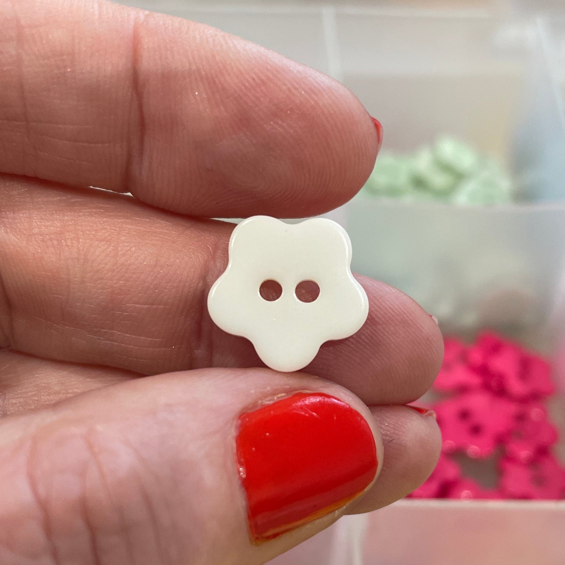 Hand holding a white button with two holes, with a colorful assortment of buttons in the background.