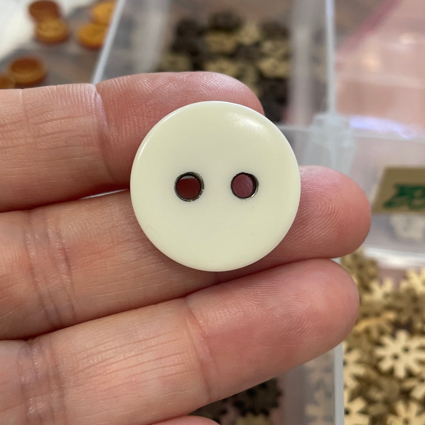 Hand holding a white button with two holes in front of a container of small buttons.