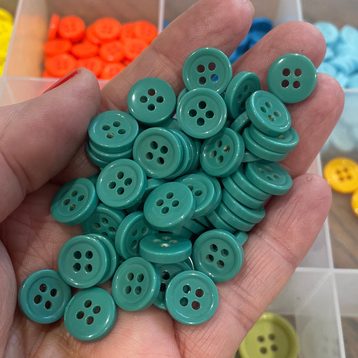 Hand holding green buttons with a background of colorful buttons in a container.