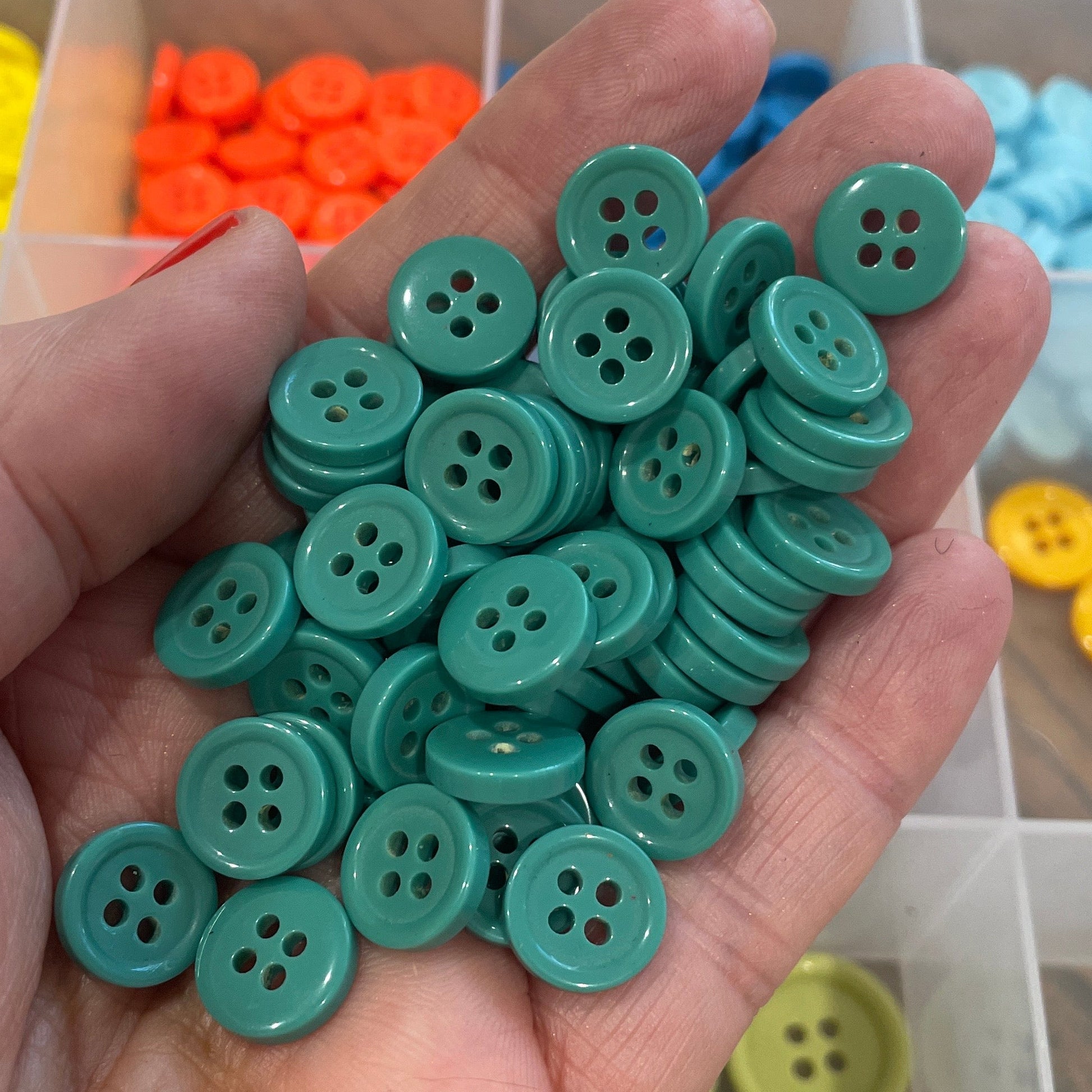 Hand holding green buttons with a background of colorful buttons in a container.