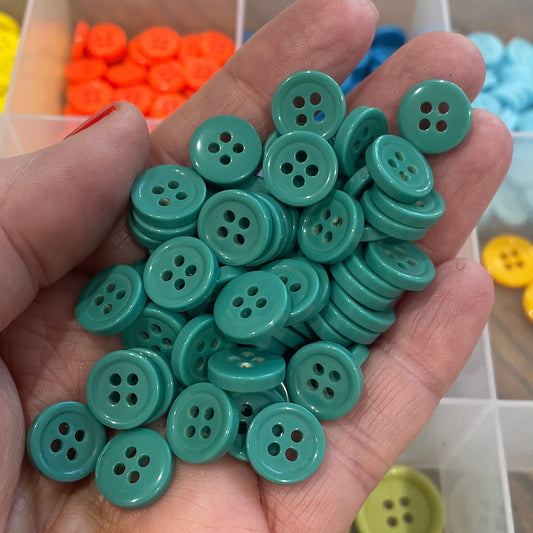 Hand holding green buttons with a background of colorful buttons in a container.