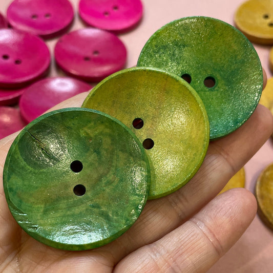Hand holding green buttons with a background of assorted colorful buttons