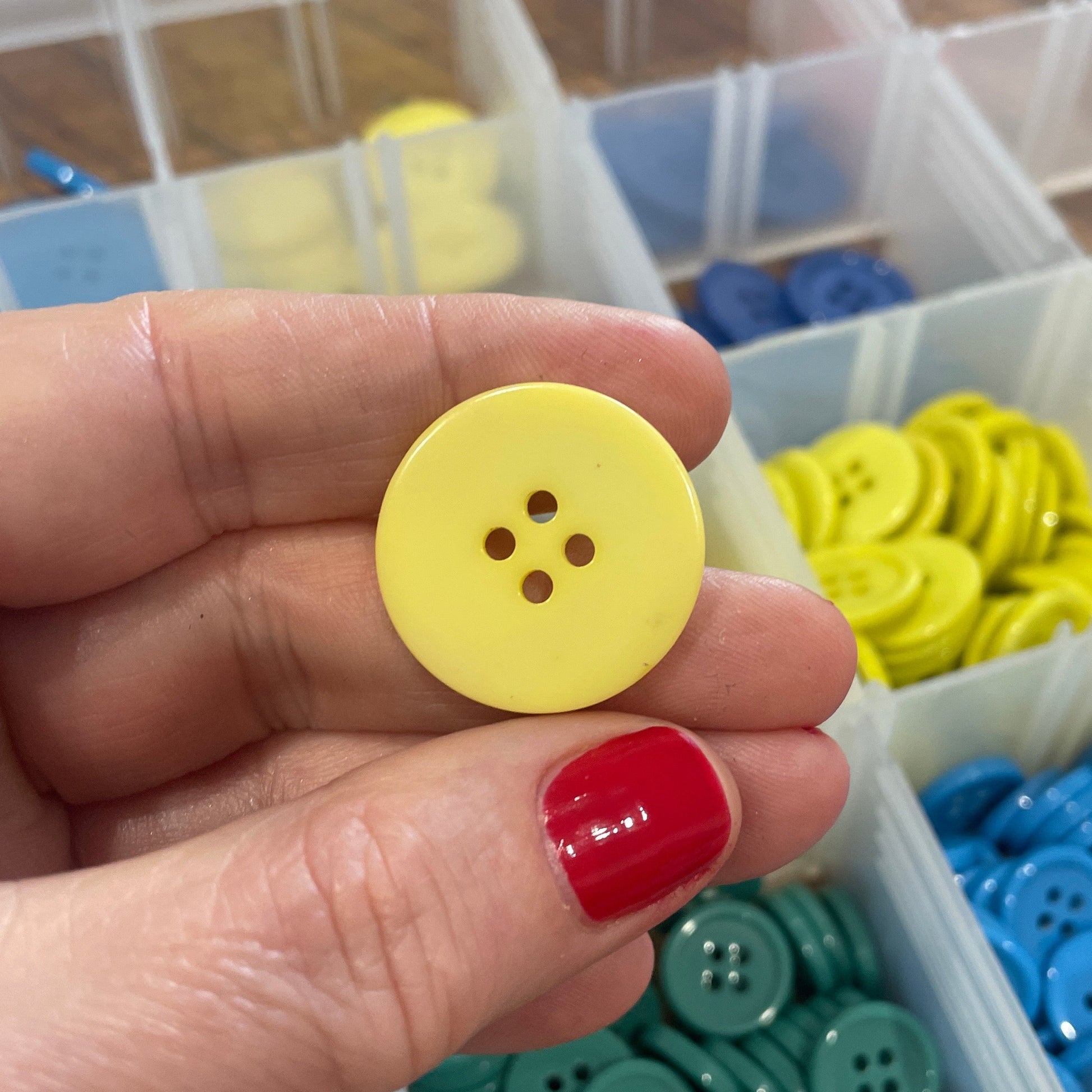 Hand holding a yellow button with a container of colorful buttons in the background