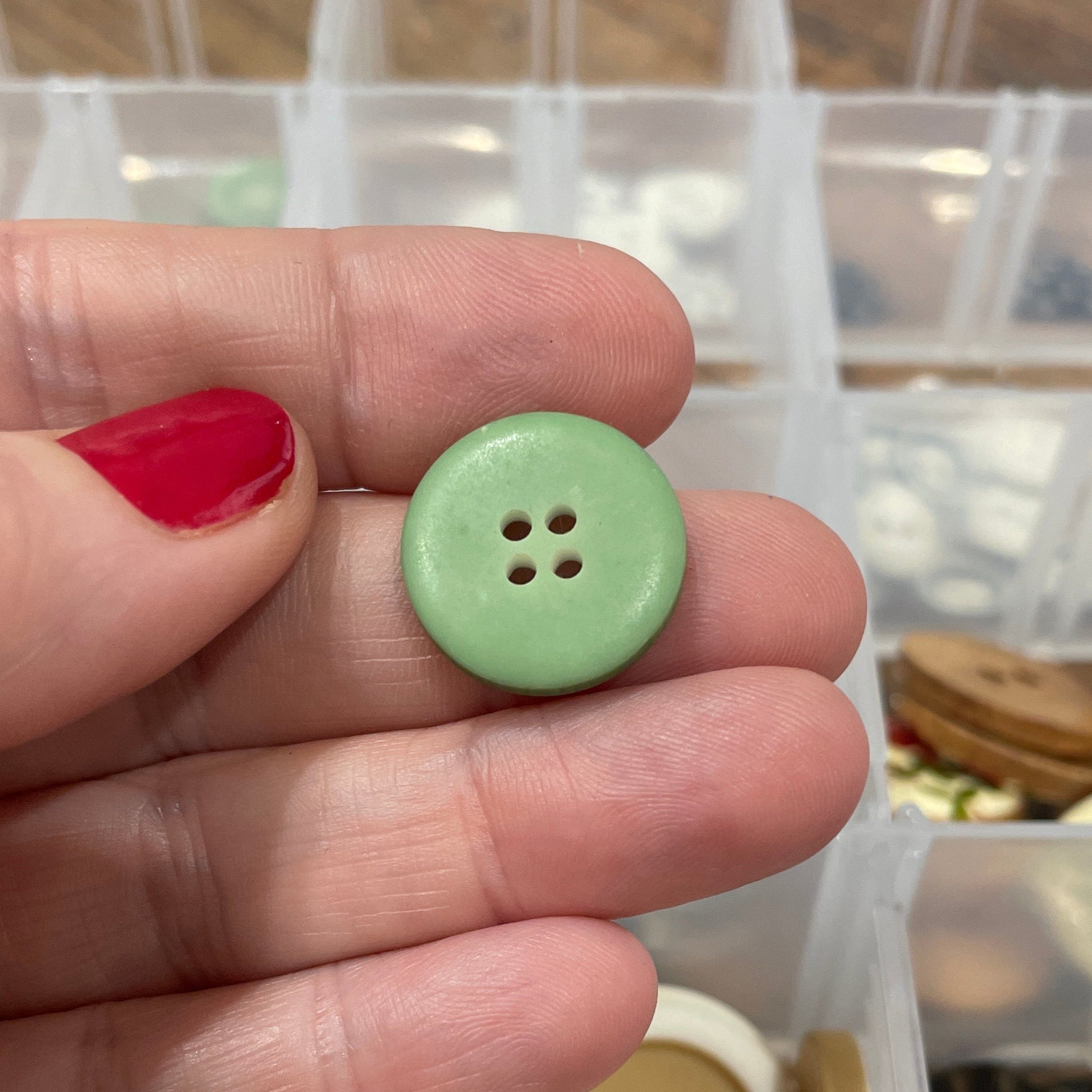Hand holding a green button with a container of buttons in the background