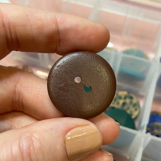 Hand holding a brown button with a container of buttons in the background