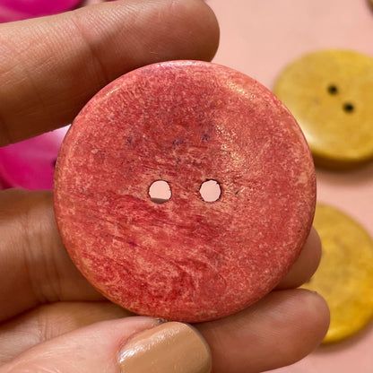 Hand holding a pink button with a collection of colorful buttons in the background