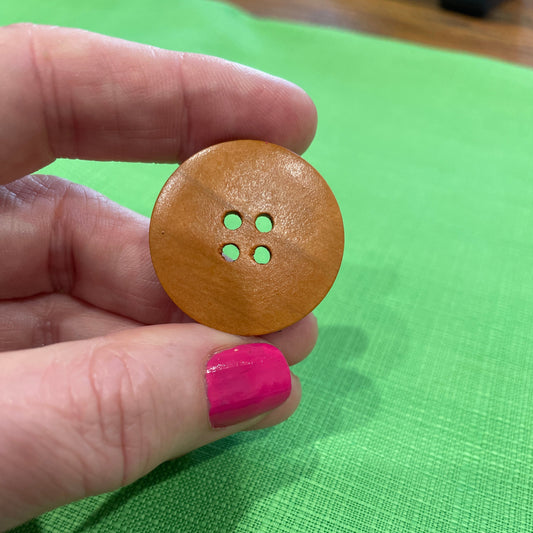 Wooden button held between fingers against a green background