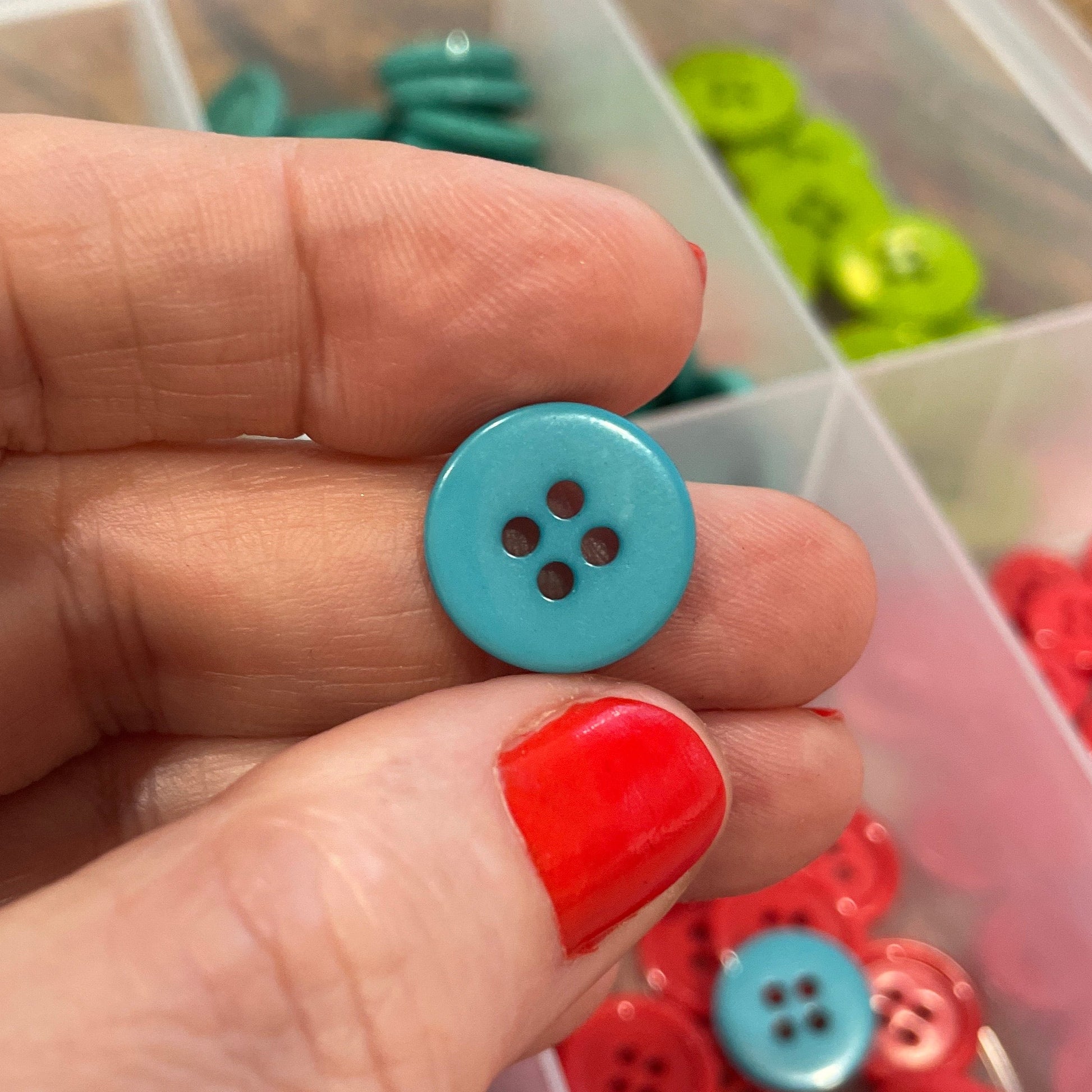 Hand holding a blue button with a container of buttons in the background