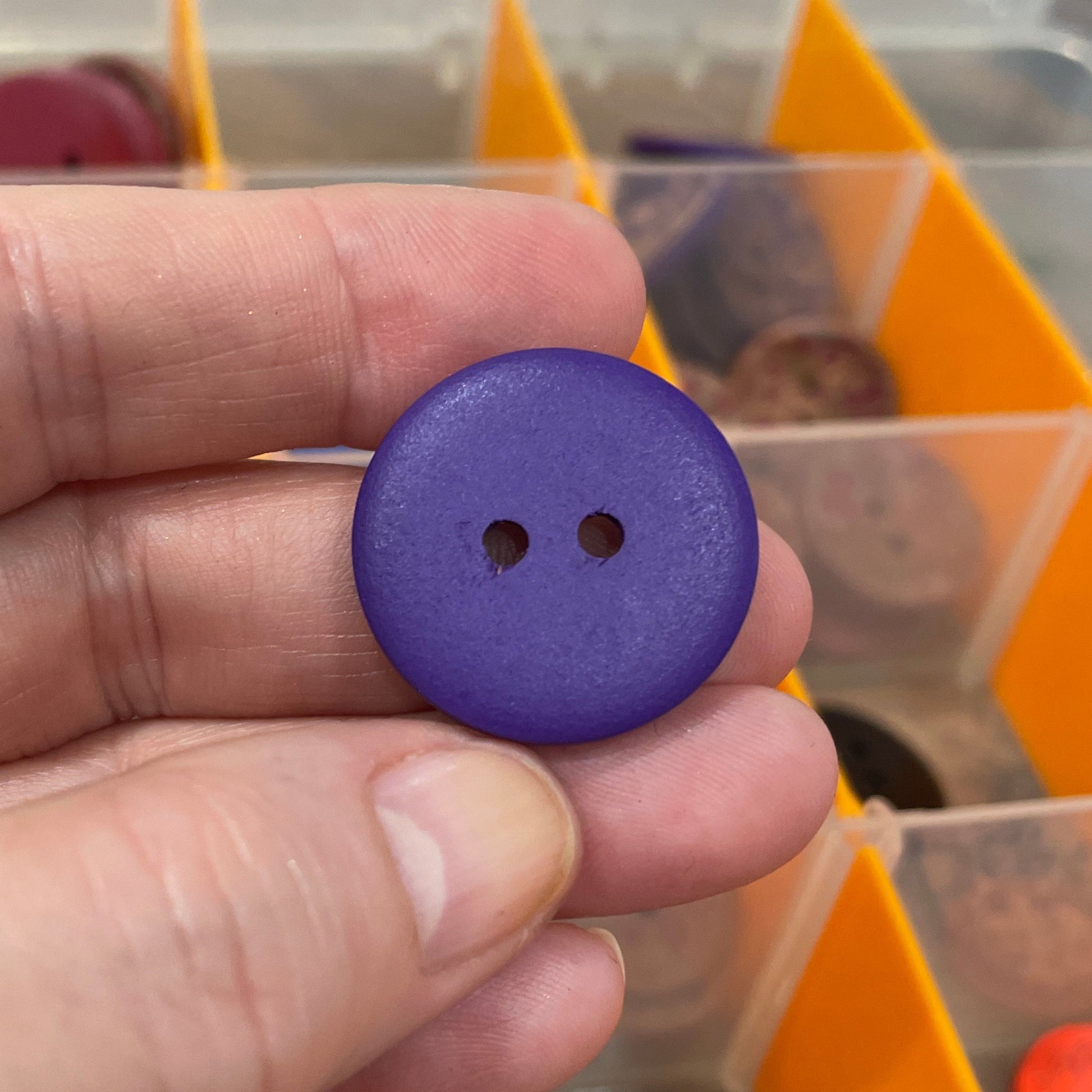 Hand holding a purple button with a background of colorful buttons in a container.