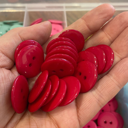 Hand holding red buttons with a blurred background of more buttons and containers.