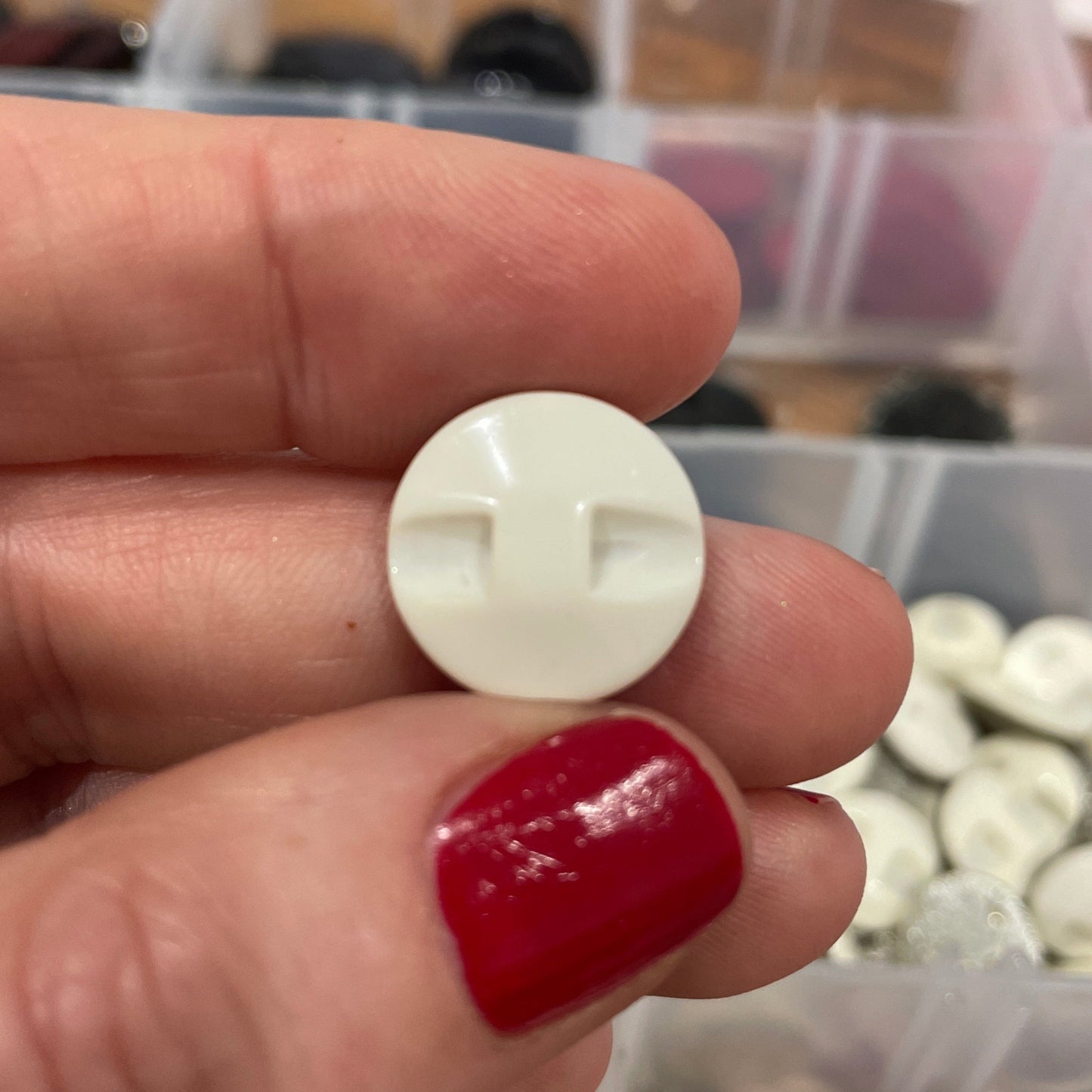 Hand holding a white button with a cross design against a blurred background of colorful buttons.