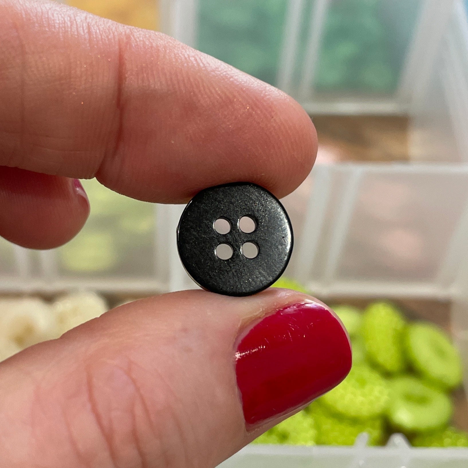Person holding a black button with four holes in front of a container of buttons.