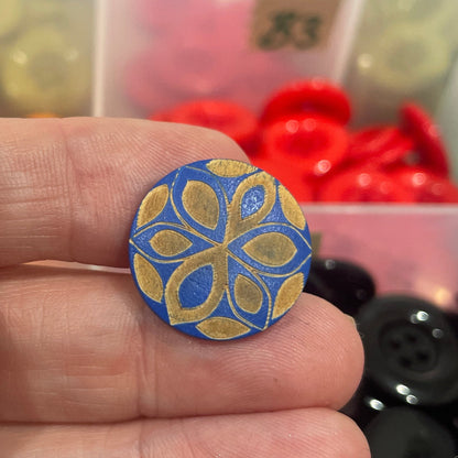 Hand holding a blue decorative button with a colorful button collection in the background.