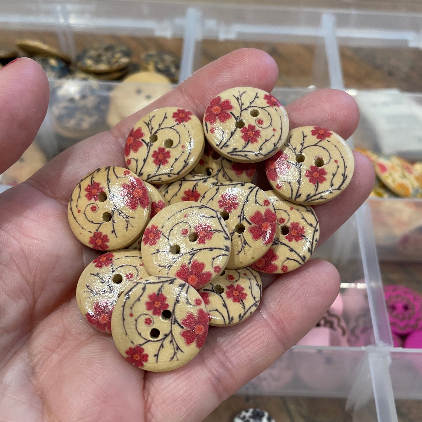 Hand holding decorative buttons with floral patterns in a craft setting