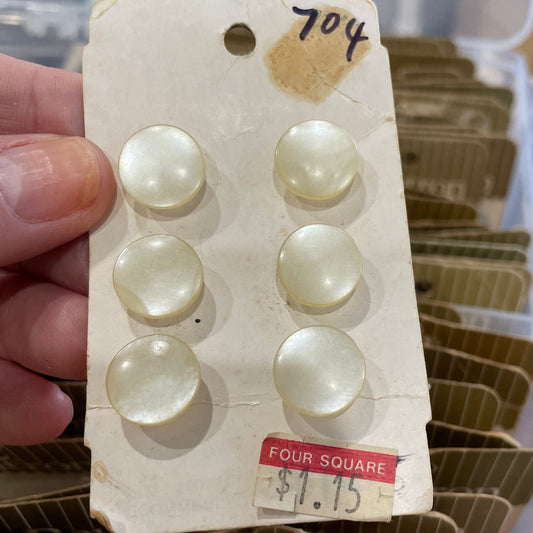 Set of pearl buttons on a card held by a hand, with a clear plastic container in the background.