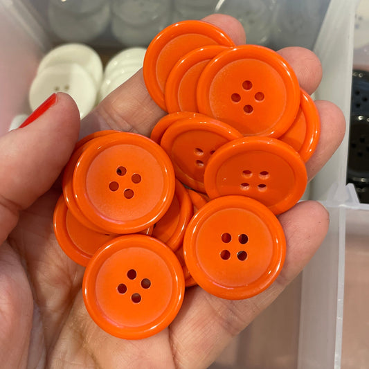Hand holding orange buttons with a container of black and white buttons in the background