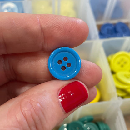 Hand holding a blue button with a container of buttons in the background