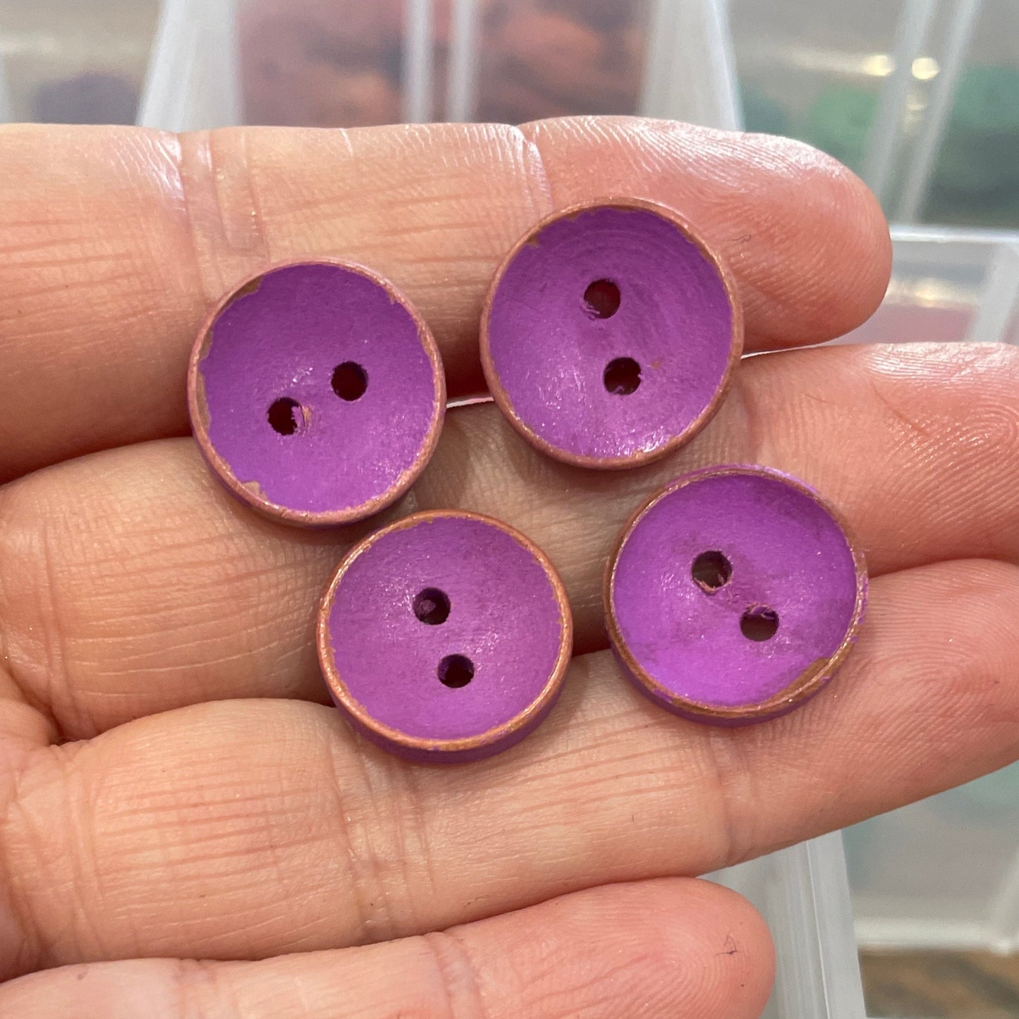 Hand holding purple buttons with a clear container of buttons in the background.