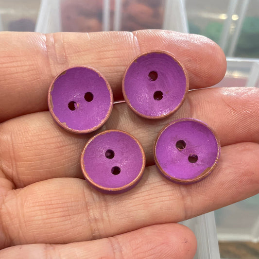 Hand holding purple buttons with a clear container of buttons in the background.