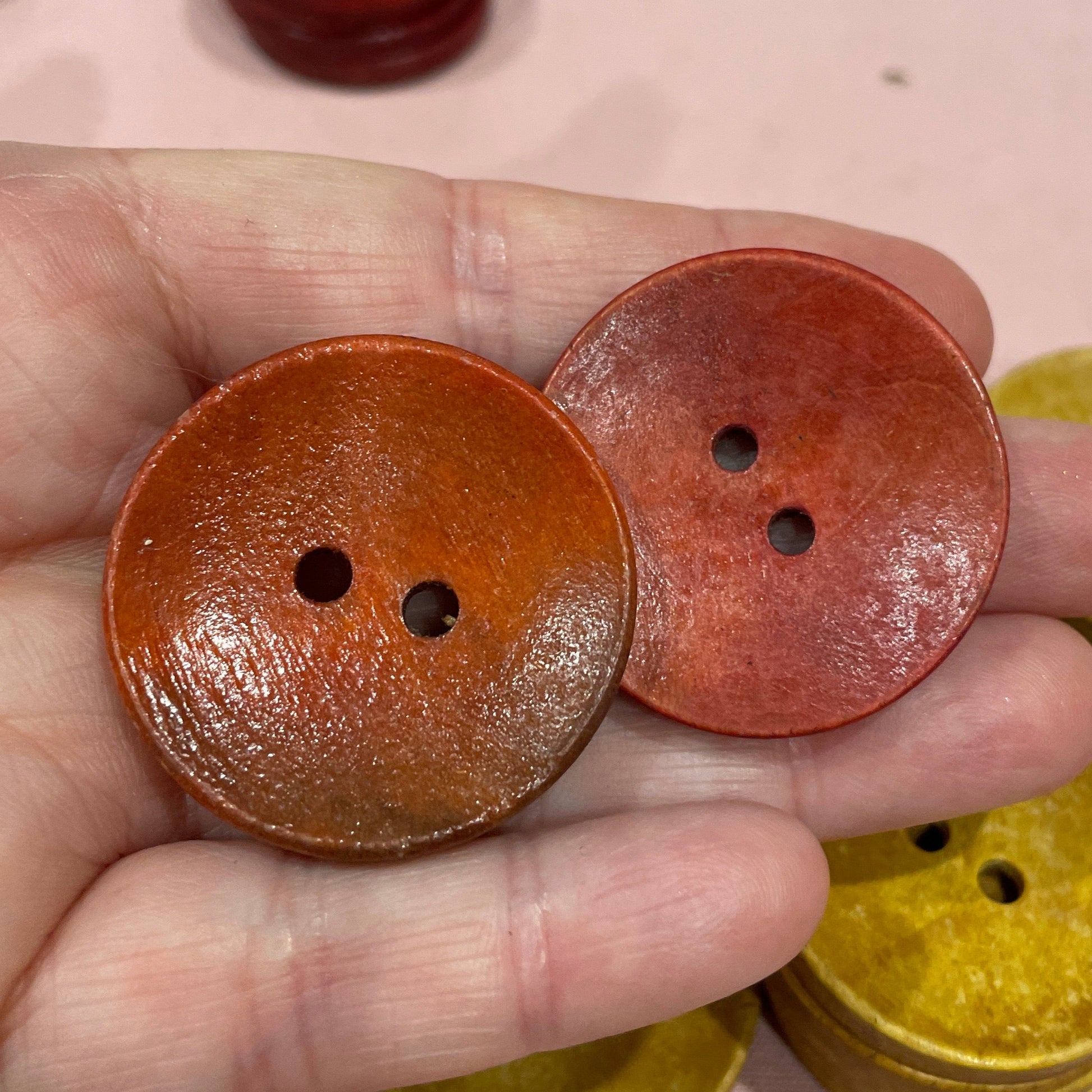 Hand holding two brown buttons with a keyboard in the background