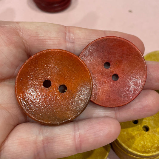 Hand holding two brown buttons with a keyboard in the background