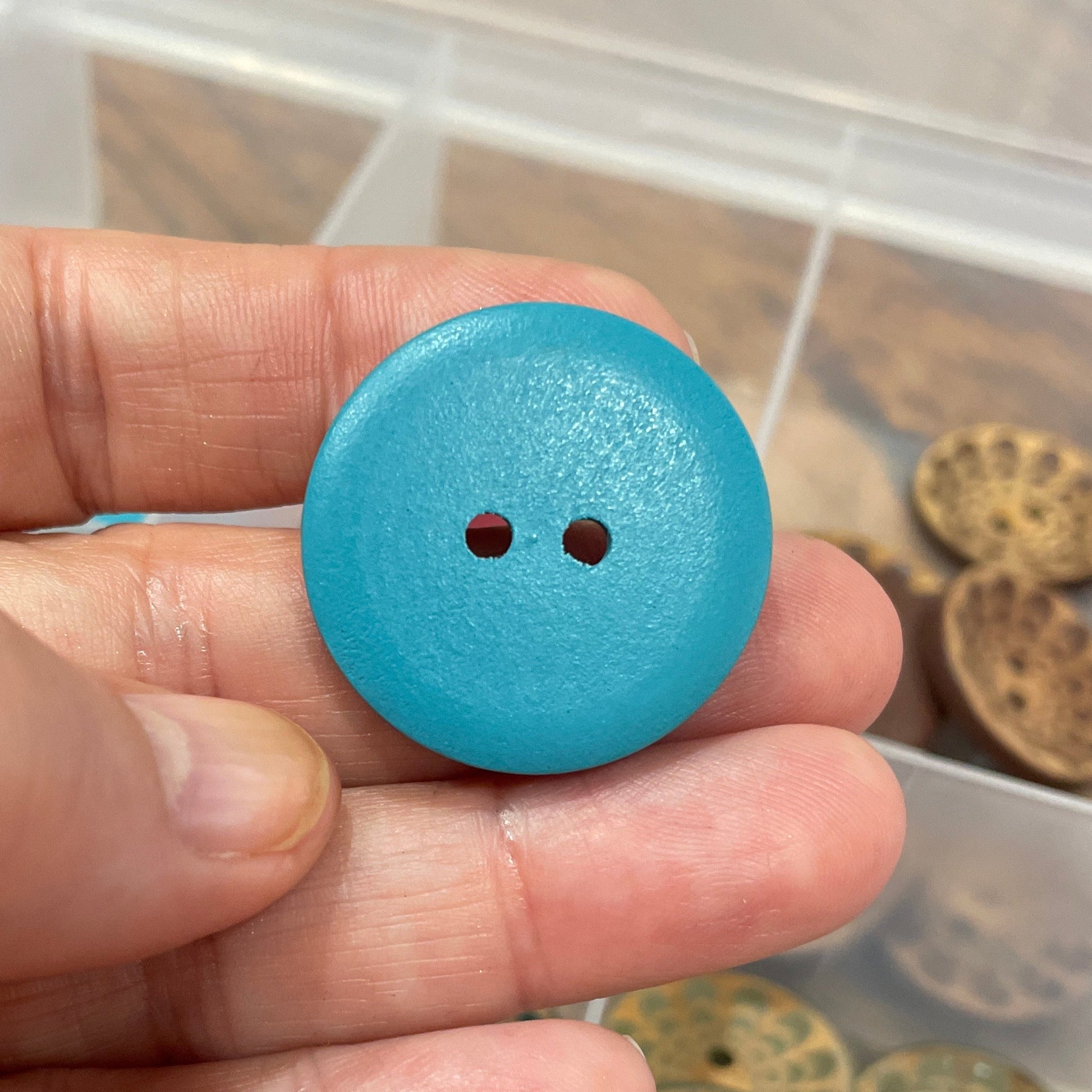 Hand holding a blue button with a container of other buttons in the background