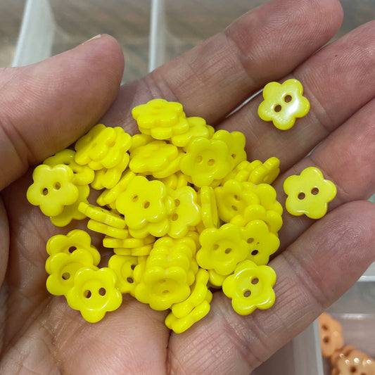 Hand holding yellow flower-shaped buttons with a blurred background of more buttons.
