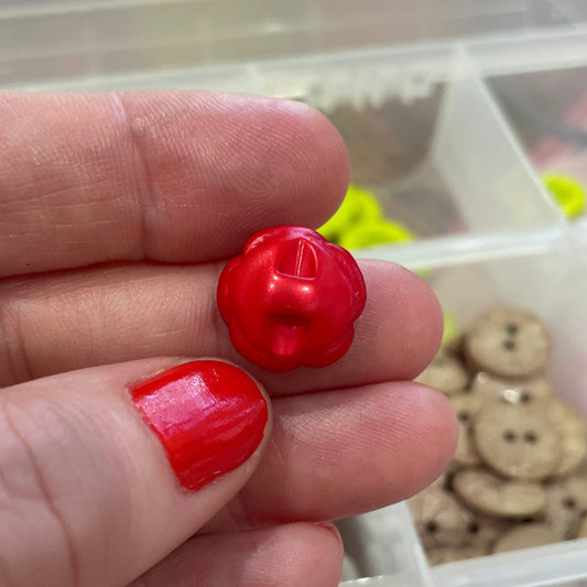 Red buttons held between fingers with a container of buttons in the background