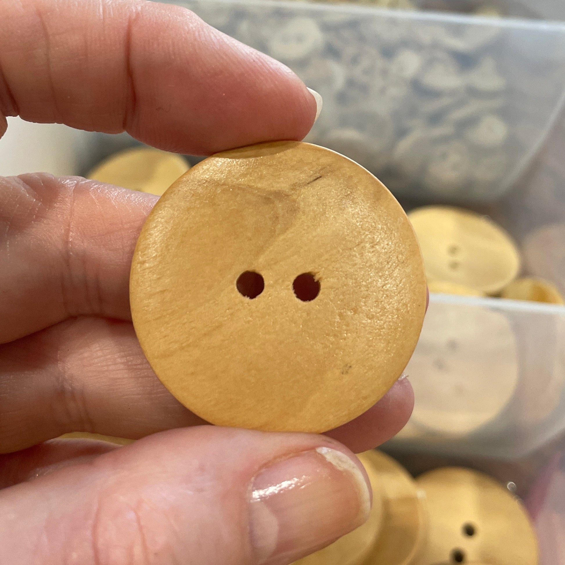 Hand holding a wooden button with a clear container of buttons in the background