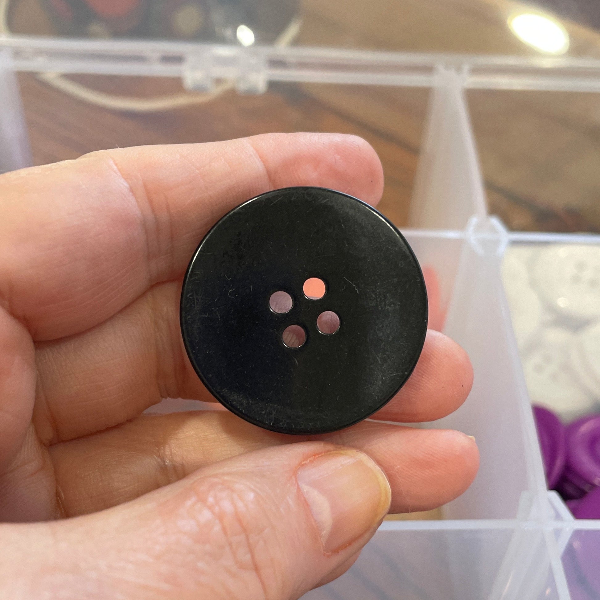 Black button held in a hand with a container of buttons in the background