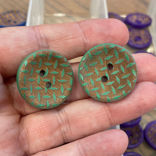 Hand holding two green buttons with a container of various buttons in the background