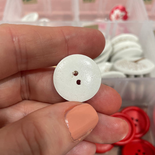 White button held between fingers with a container of buttons in the background
