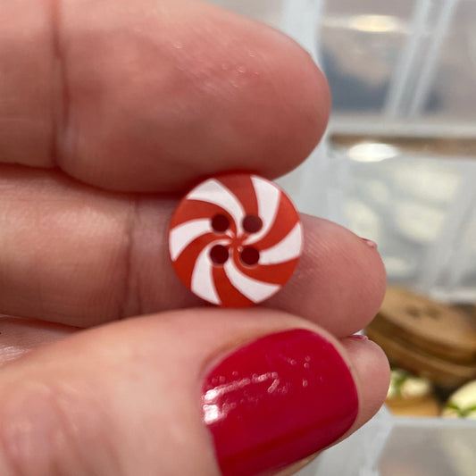 Hand holding a red and white button with a container of buttons in the background
