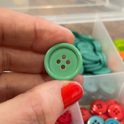 Hand holding a green button with a container of buttons in the background