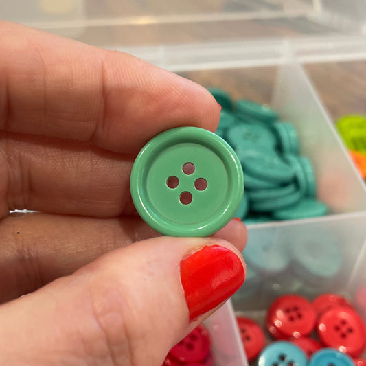 Hand holding a green button with a container of buttons in the background