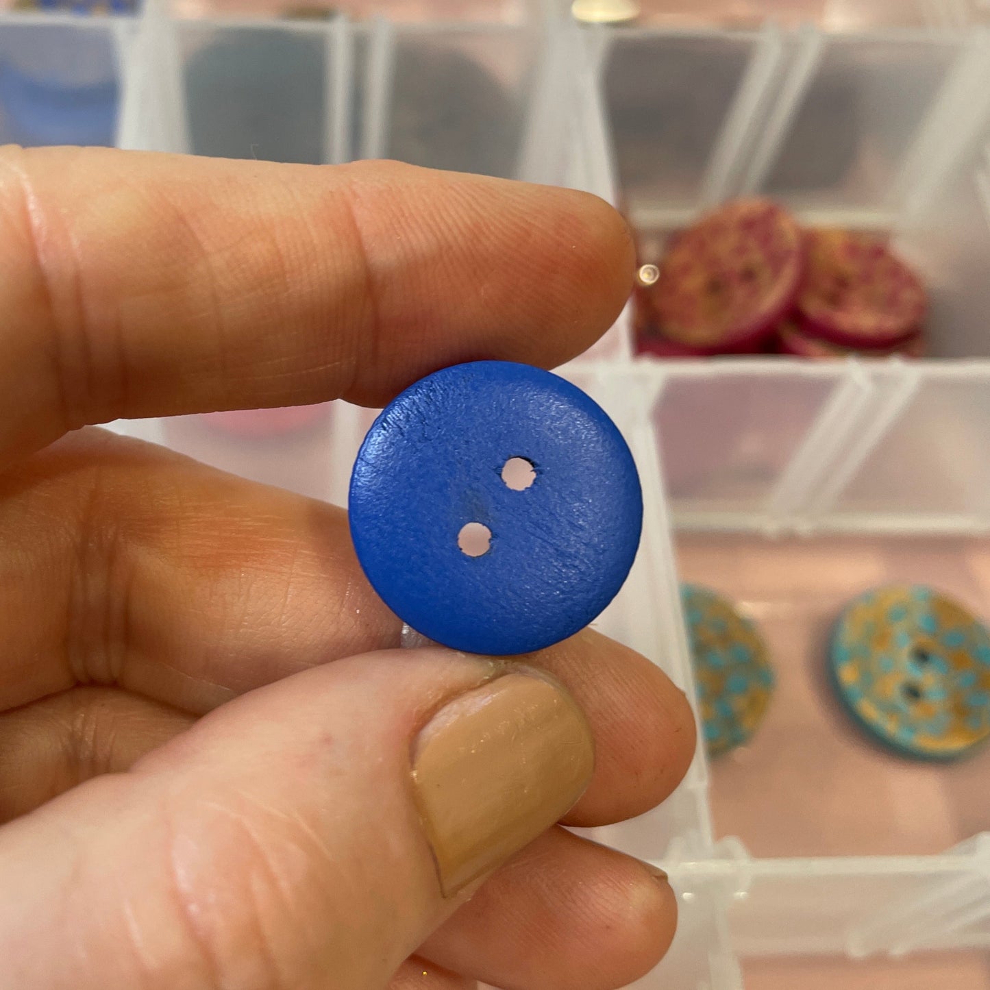 Hand holding a blue button with a container of buttons in the background