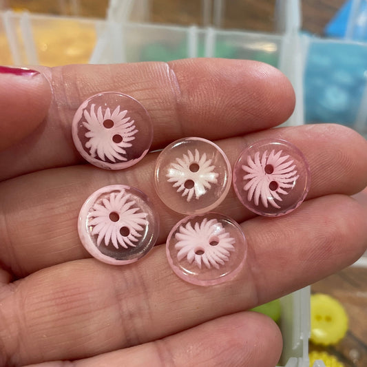 Hand holding pink buttons with a blurred background of a storage box with more buttons.
