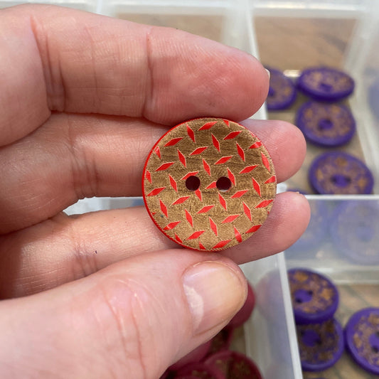 Hand holding a decorative button with a container of buttons in the background