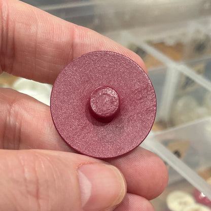 Hand holding a round button with a container of assorted colored objects in the background