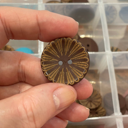 Hand holding a decorative button with a clear container of assorted buttons in the background