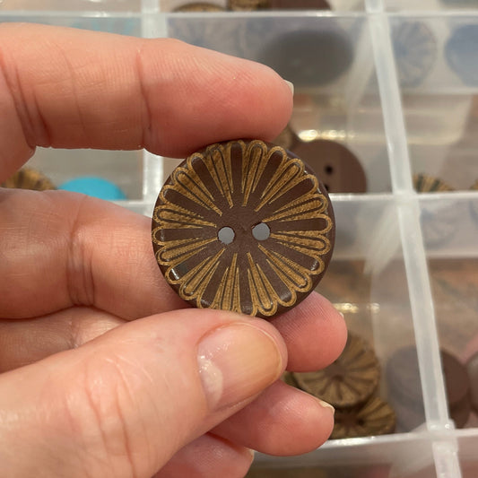 Hand holding a decorative button with a clear container of assorted buttons in the background