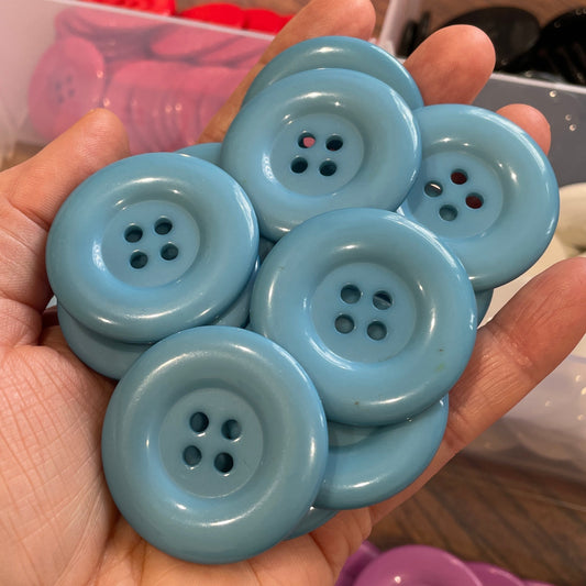 Hand holding blue buttons with a container of buttons in the background