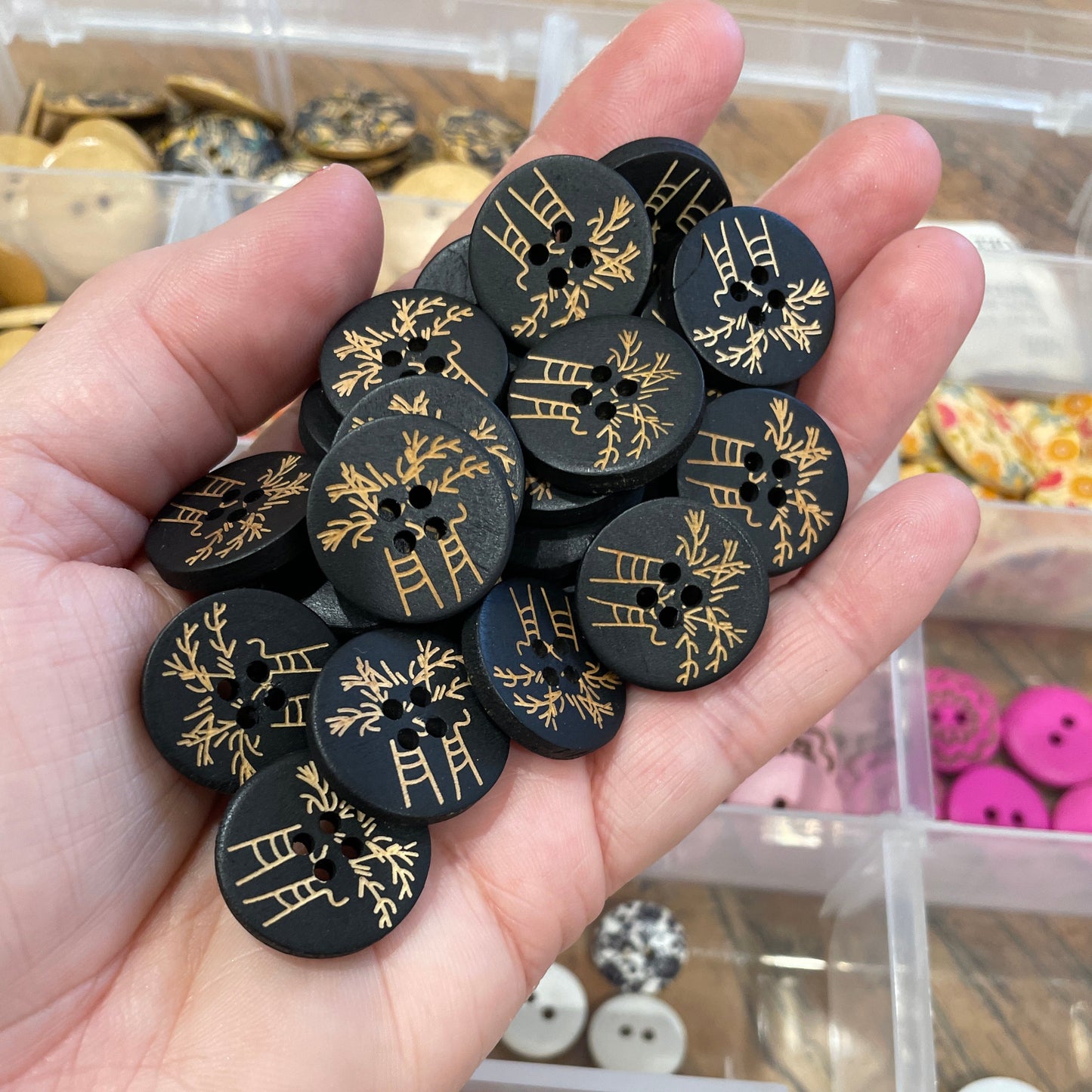 Hand holding black buttons with gold patterns against a blurred background of more buttons.