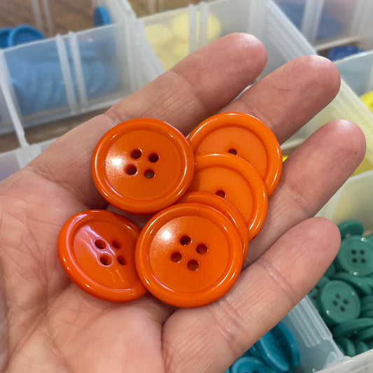 Hand holding orange buttons with a container of buttons in the background