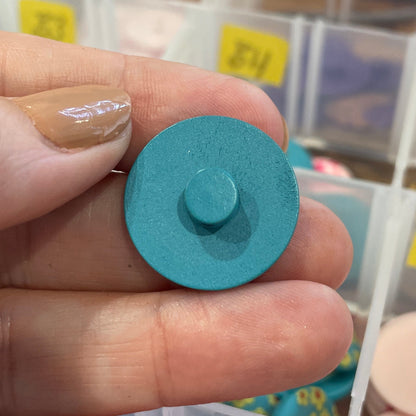 Hand holding a blue button with a background of assorted buttons in containers