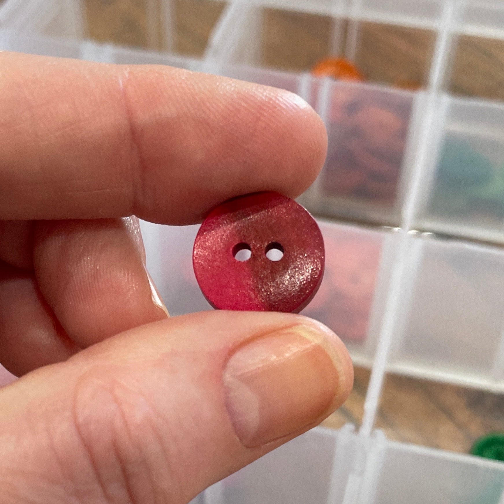 Hand holding a red button with a clear container of buttons in the background