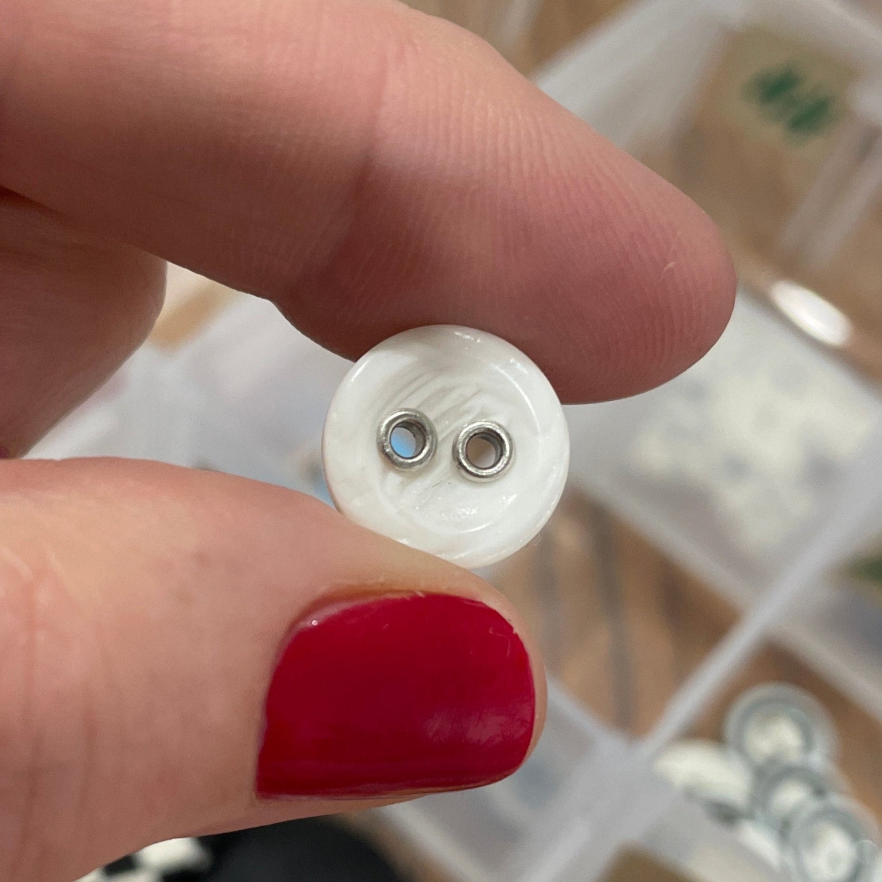 Hand holding a white button with a blurred background of a button collection.